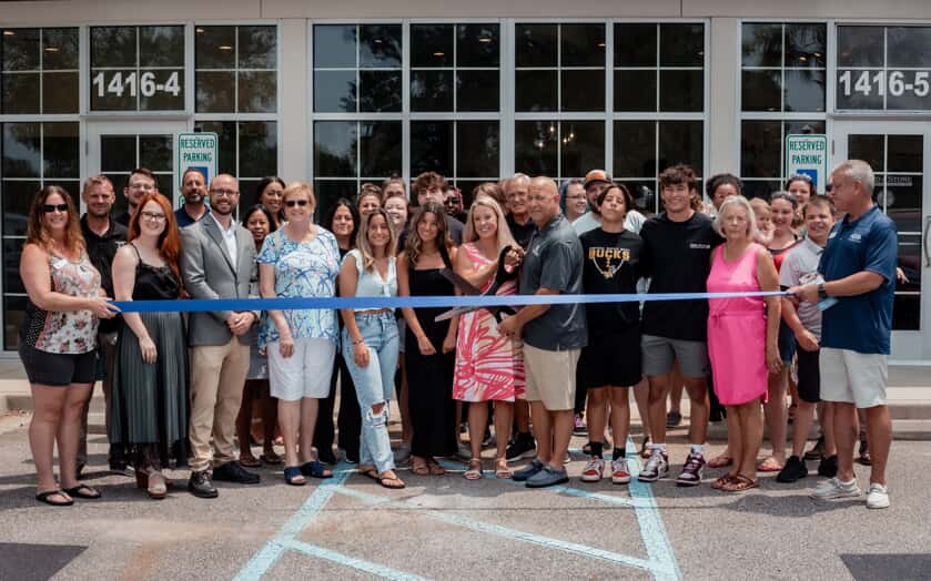 Franchise owners and group of employees and family standing in front of new storefront for ribbon cutting ceremony