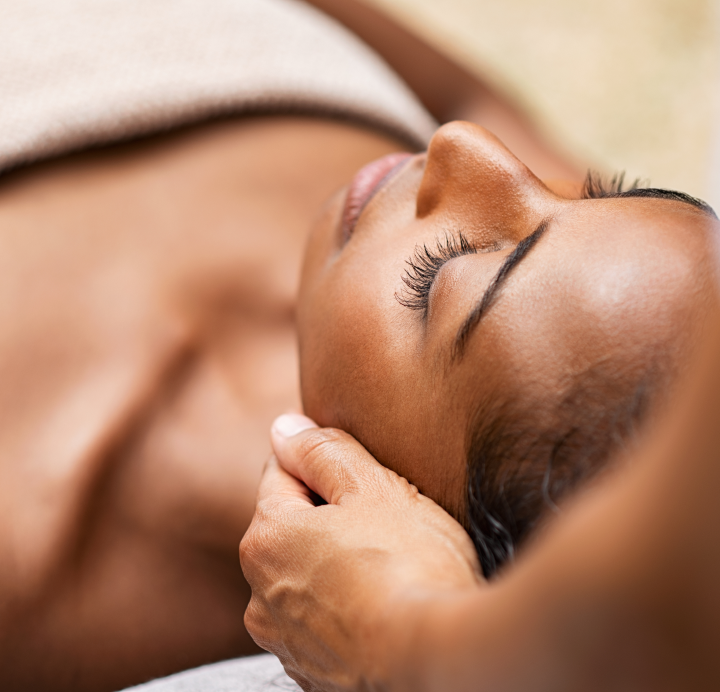 a technician's hands touching a black woman's face during a massage.