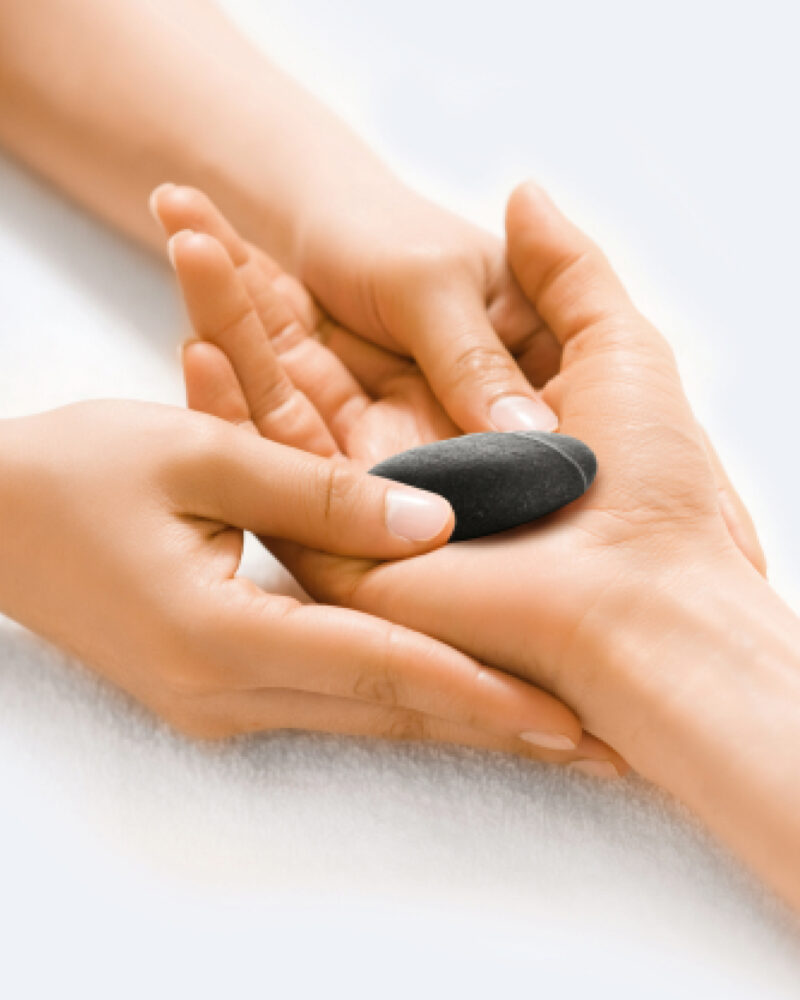 A masseuse's hands placing a black stone into a woman's palm.