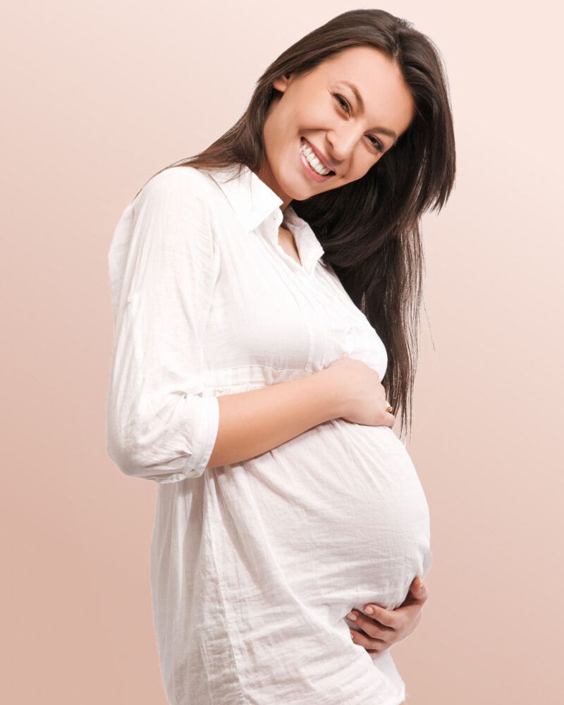 A pregnant white woman in a white linen dress showing her baby bump from the side.