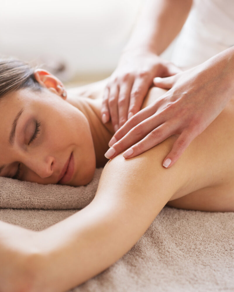 A masseuse's hands rubbing a white woman's shoulder.